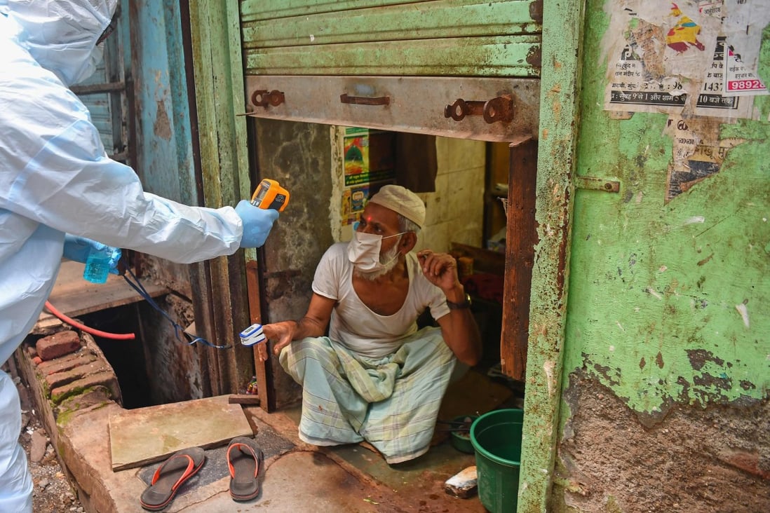 Medical staff wearing personal protective equipment take the temperature of a man as they conduct door-to-door Covid-19 screening inside the Dharavi slum in Mumbai. Photo: AFP