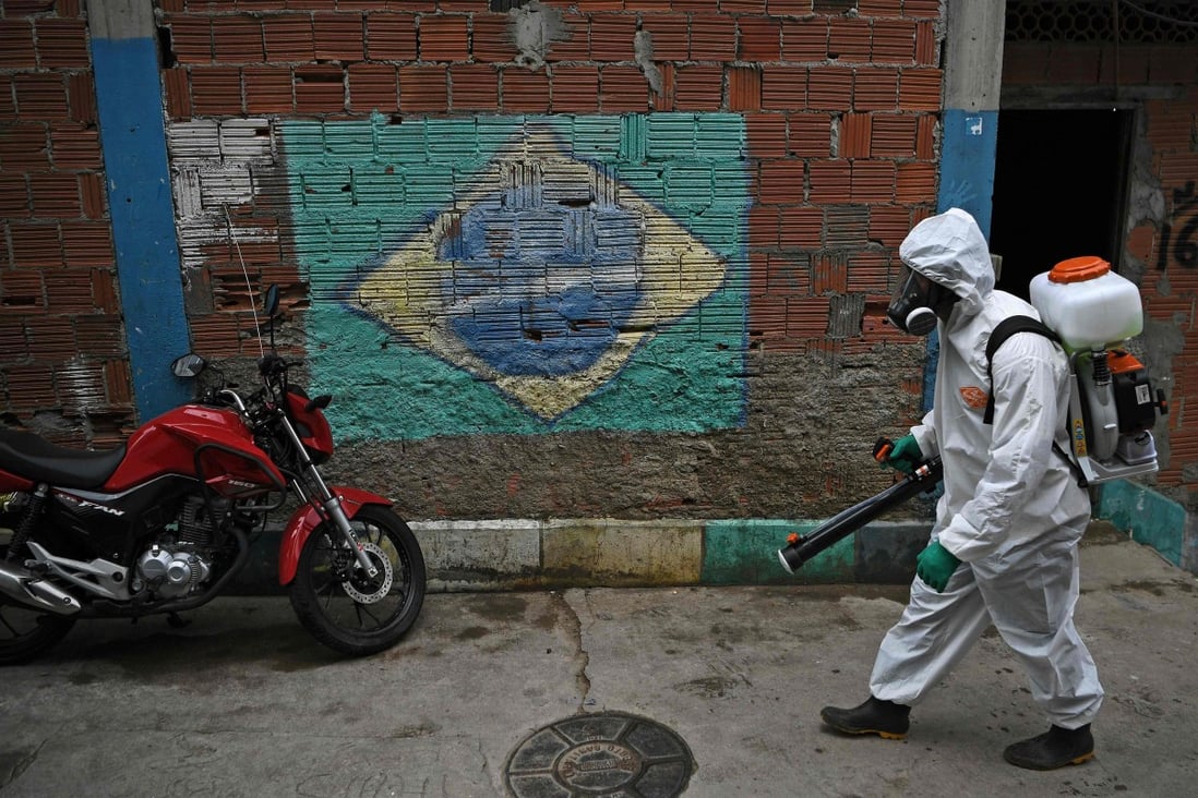 A volunteer walks past a mural of the Brazilian flag as he disinfects an area at the Babilonia favela, in Rio de Janeiro. Photo: AFP