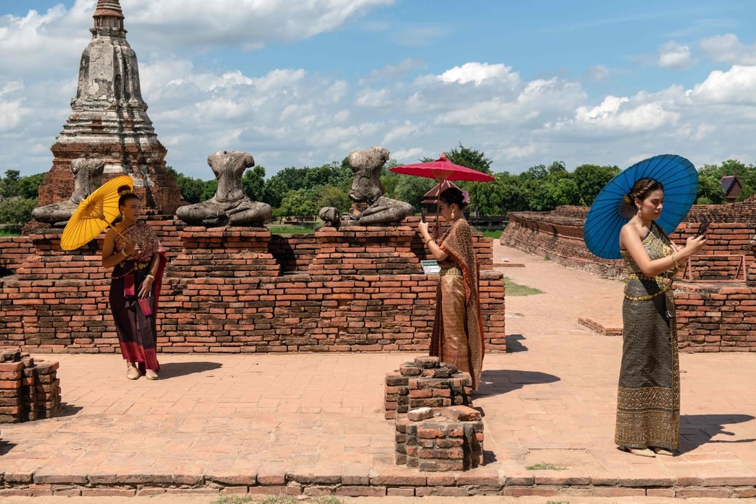 Visitors carry sun umbrellas as they pose for photos at the 17th century Wat Chaiwatthanaram temple complex north of Bangkok after authorities reopened tourists sites earlier this month. Photo: AFP