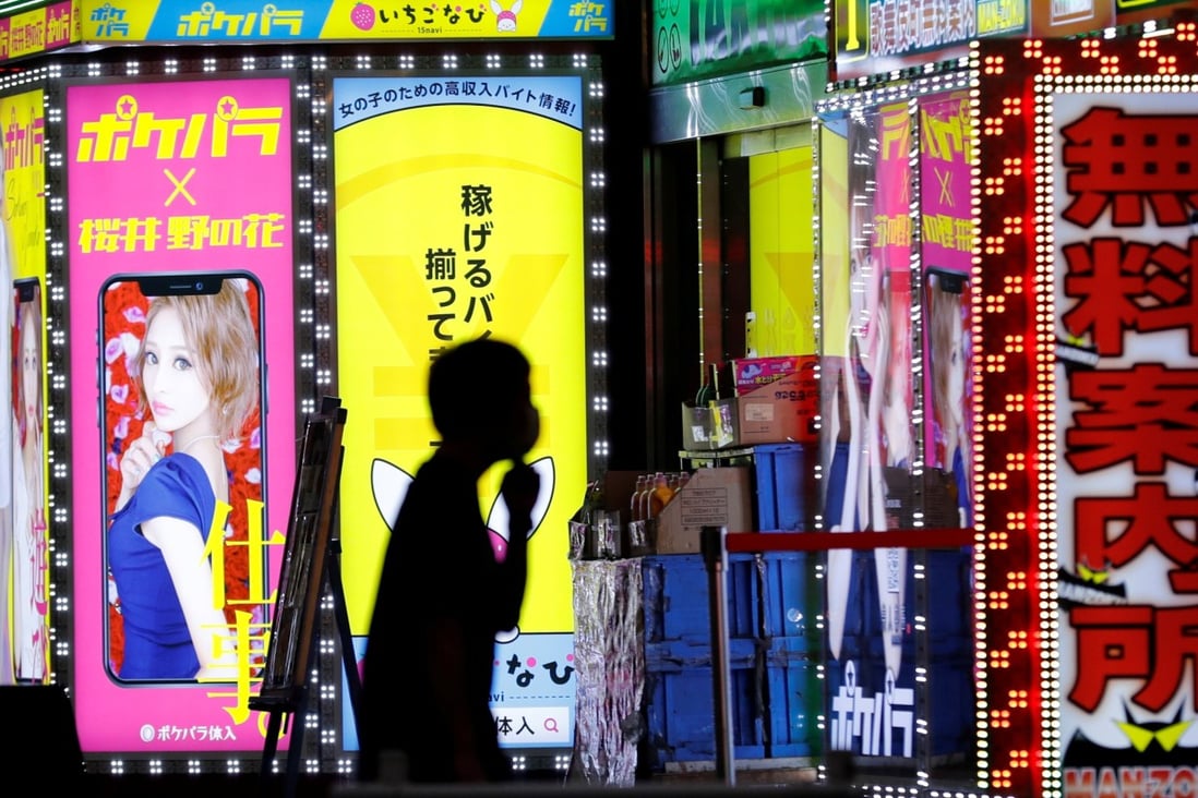 A man wearing a face mask walks past signboards for bars in Tokyo’s Shinjuku district. Photo: Reuters