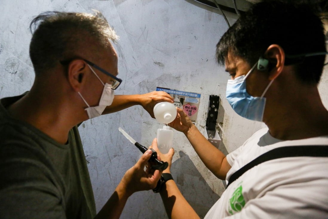 Build & Wish team members Hin and Gary (left to right), fill a hand sanitiser dispenser they installed at a housing estate in Sham Shui Po. Photo: Jonathan Wong