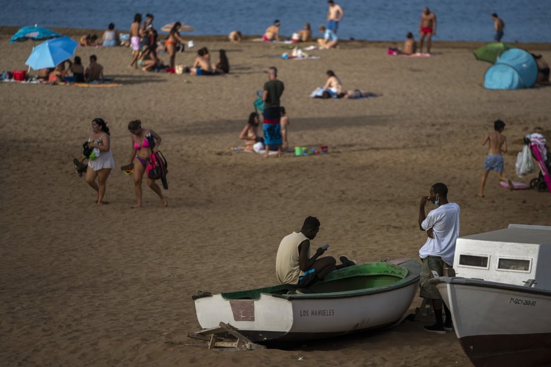 Two migrants sit on a fishing boat as people enjoy the beach on Gran Canaria island last month. Photo: AP