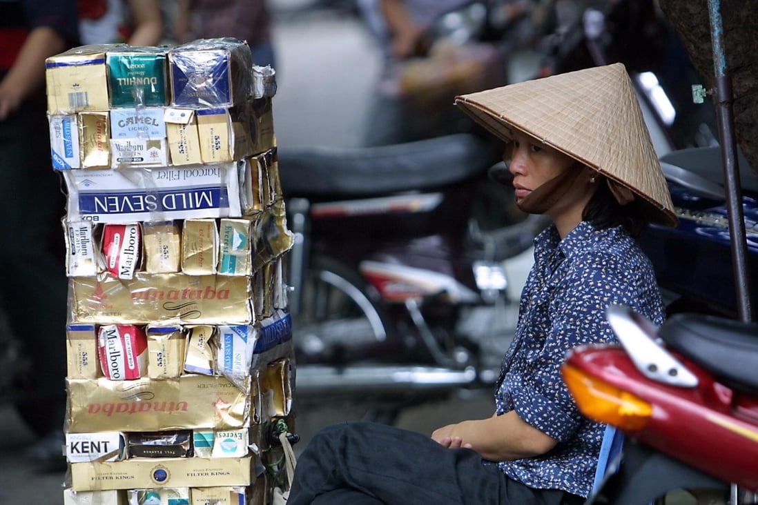 A cigarette vendor sits behind a pile of empty cartons of foreign and local cigarette brands on a Hanoi street on May 31. Vietnamese smokers can easily buy foreign brands at low prices thanks to persistent cigarette smuggling carried out through Vietnam’s borders with Laos, Cambodia and China. Photo: AFP