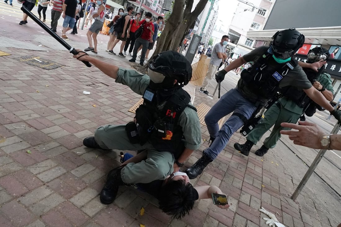 A police officer points with his baton as he holds down an anti-government protester during an illegal demonstration in July. Photo: Felix Wong