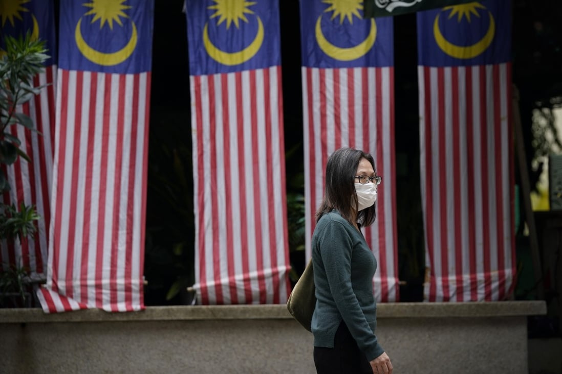 A Malaysian woman wearing a face mask crosses a street draped with national in Kuala Lumpur. Photo: AP