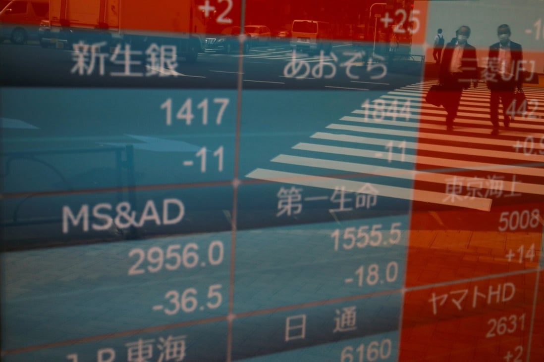 Passersby wearing protective face masks are reflected on a stock quotation board outside a brokerage in Tokyo, Japan. Photo: Reuters