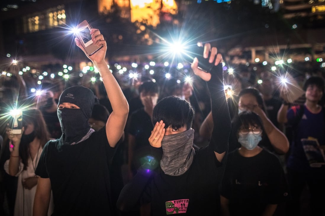 Secondary school students wave their phones and cover an eye in support of a woman who was injured, during an anti-government rally in Central, Hong Kong, on August 22, 2019. Photo: EPA-EFE