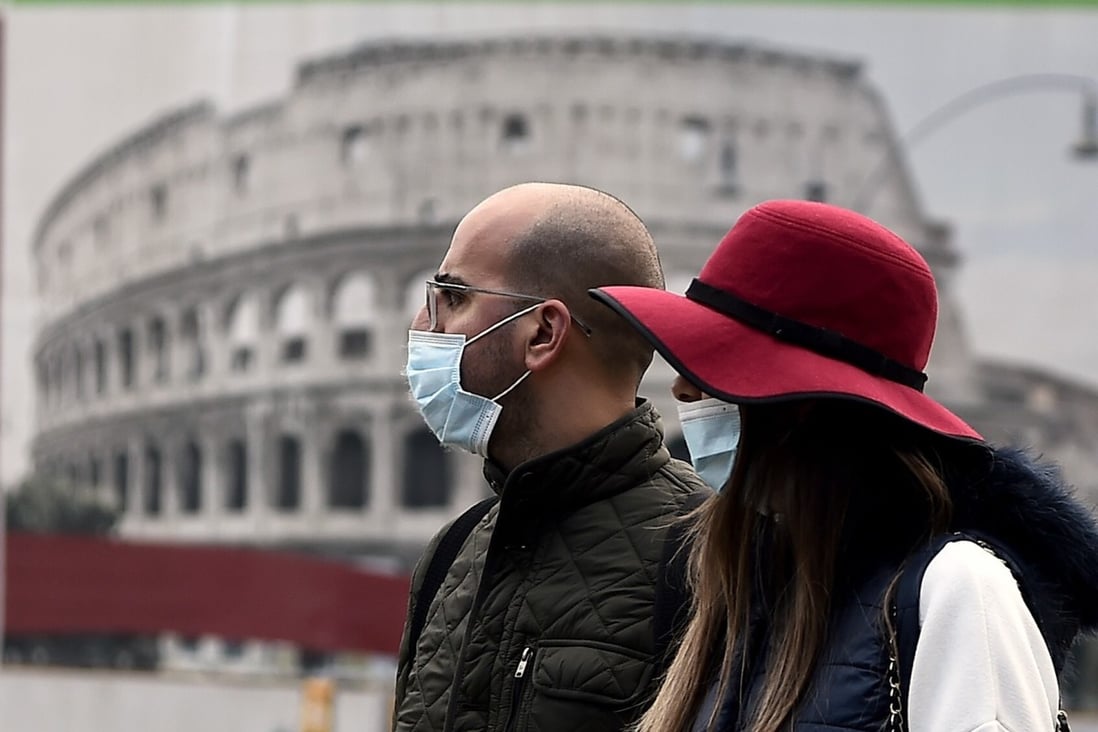 A couple wearing face masks walk past a poster representing the Colosseum in l Rome on Tuesday. Photo: AFP