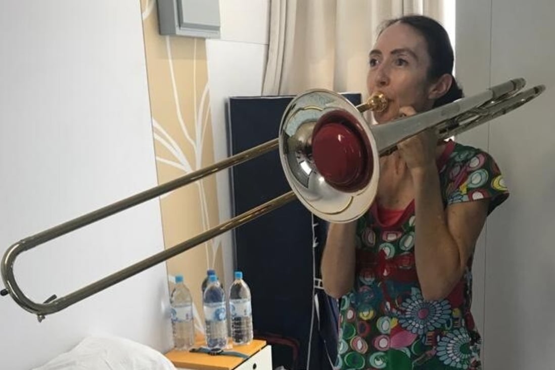 One of the Hong Kong Philharmonic’s quarantined musicians, Megan Sterling, principal flute, plays her husband’s trombone for a change in her quarantine room at Penny’s Bay, Lantau Island. Players have been practising, learning new works, and doing yoga during their confinement. Photo: Megan Sterling