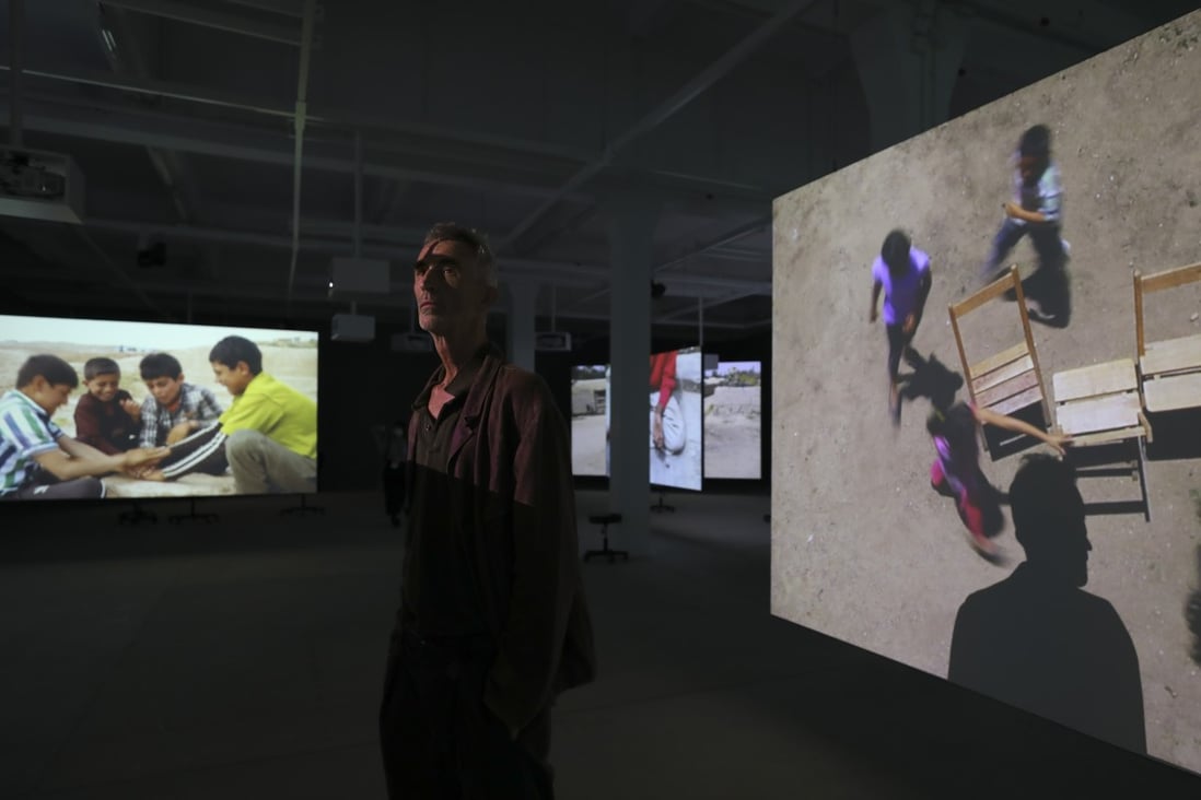 Francis Alÿs poses amid his installation “Children‘s Games”, a series of videos of children at sites of conflict playing, part of his exhibition at Tai Kwun Contemporary in Central, Hong Kong. Alÿs is a Belgian-born, Mexico-based artist. Photo: Xiaomei Chen