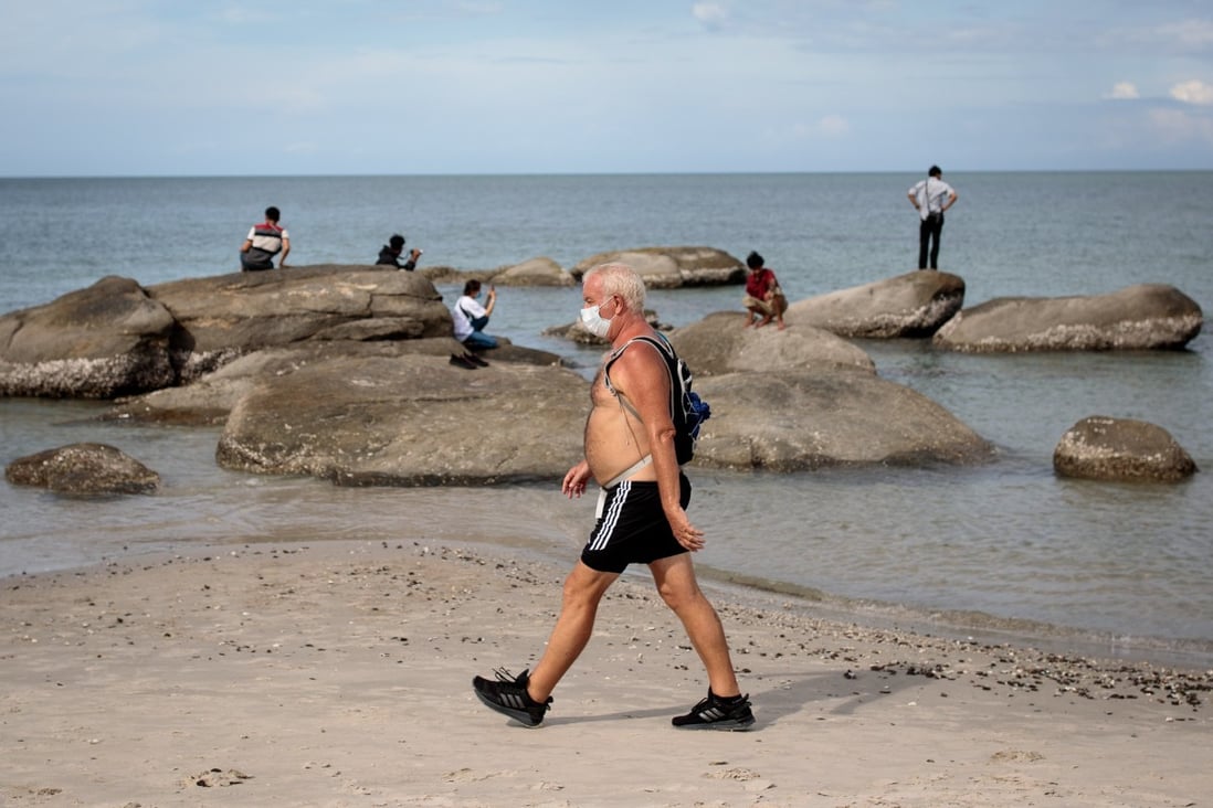 A man wearing a face mask walks along Hua Hin beach in Thailand. Covid-19 is expected to cost the global economy US$20 trillion or more. Photo: AFP