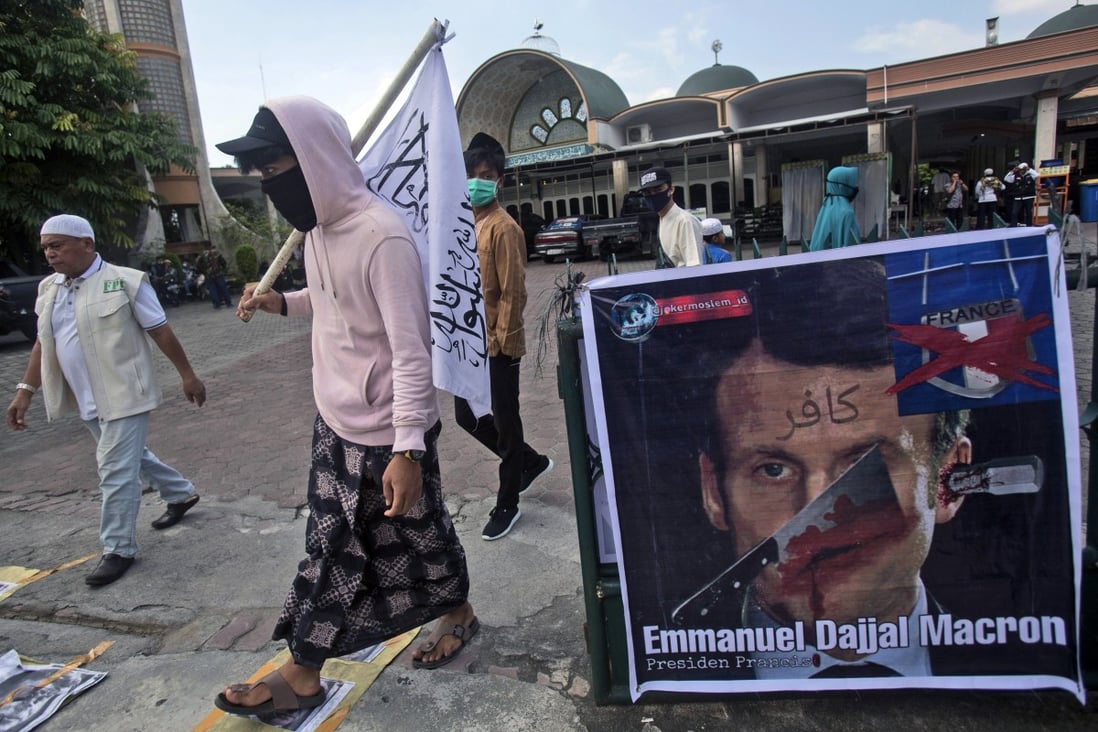 Muslim men walk past a defaced poster of French President Emmanuel Macron during a protest in Medan, North Sumatra, Indonesia on Friday. Photo: AP Photo
