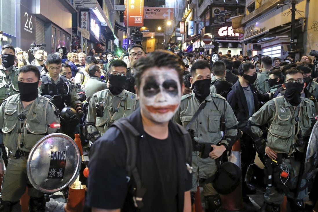 A man with his face painted like the Joker stands in front of riot police in Lan Kwai Fong on Halloween last year. Photo: AP