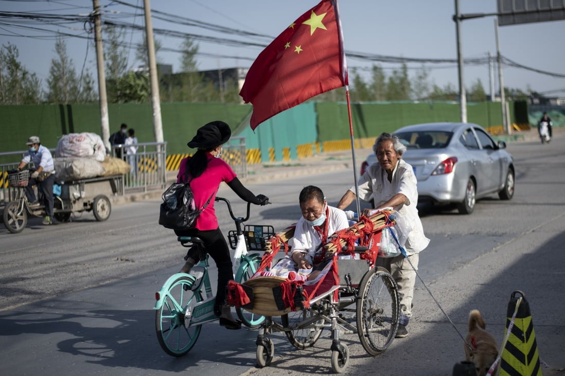 An elderly man pushes a woman wearing a face mask in a wheelchair adorned with the Chinese national flag in Beijing. The Chinese government plans to raise the retirement age, a move that has upset workers. Photo: AFP