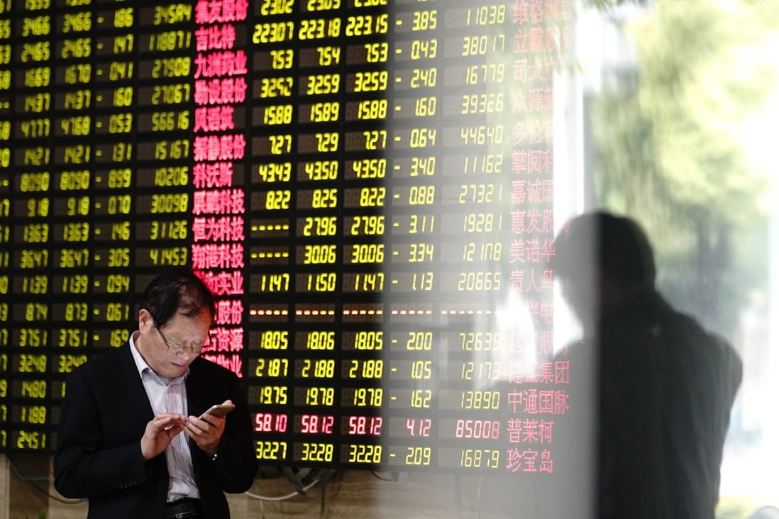 A man looks at his smartphone near a display showing stock prices at a brokerage house in Shanghai. Photo: AP Photo