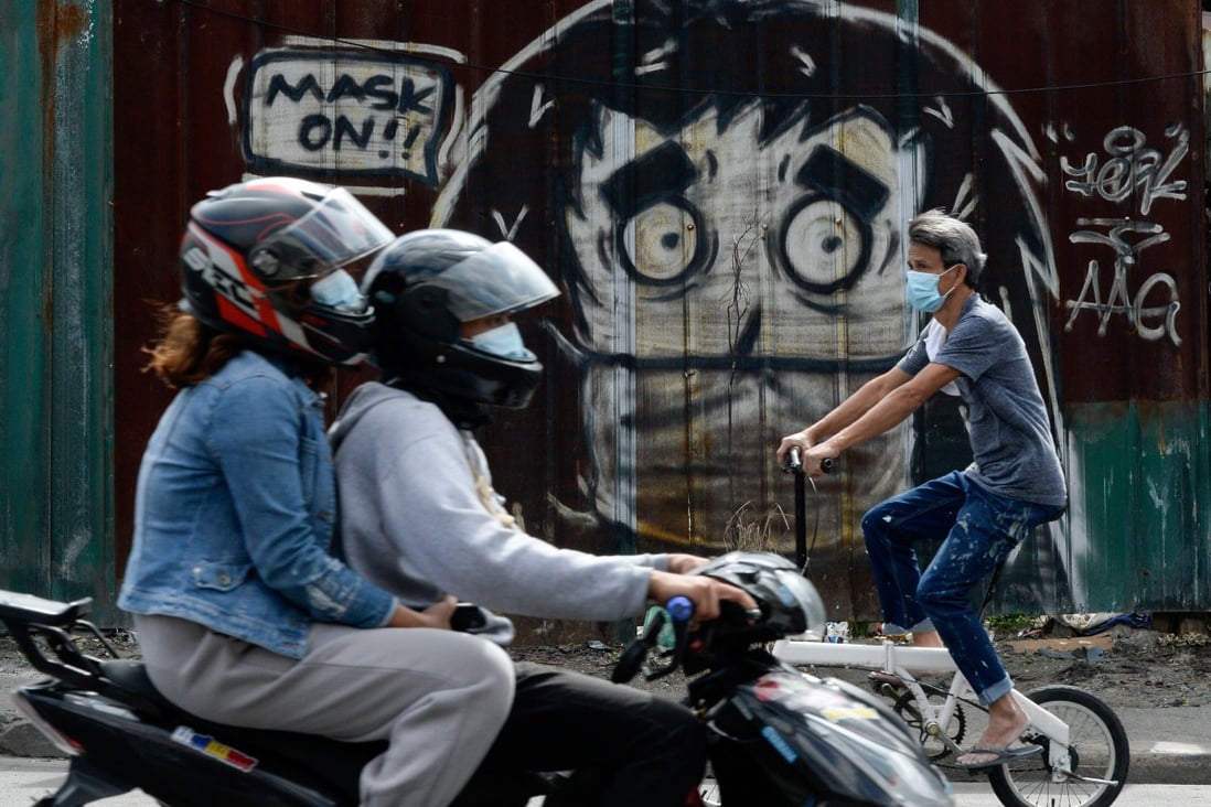 People ride past a mural reminding residents in Manila to wear face masks. Photo: Reuters
