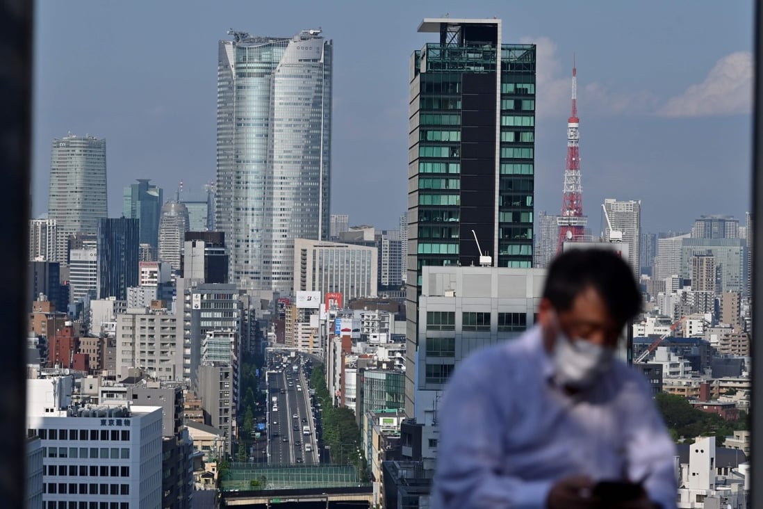 A man sitting on a rooftop checks his phone, flanked by the Tokyo skyline on June 8, 2020. A recently released survey found Tokyo was investors’ third top investment destination in the Asia-Pacific. Photo: AFP
