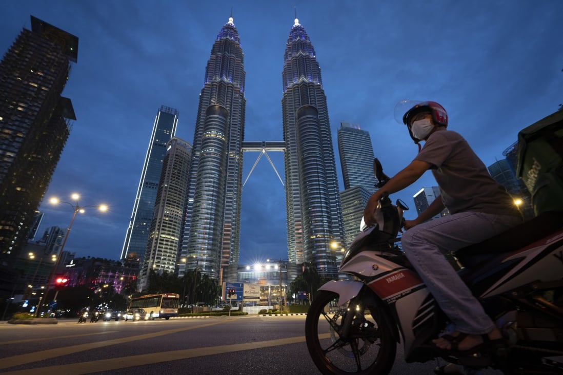 A food delivery rider waits at a traffic junction in front of Kuala Lumpur’s Petronas Twin Towers. Photo: AP