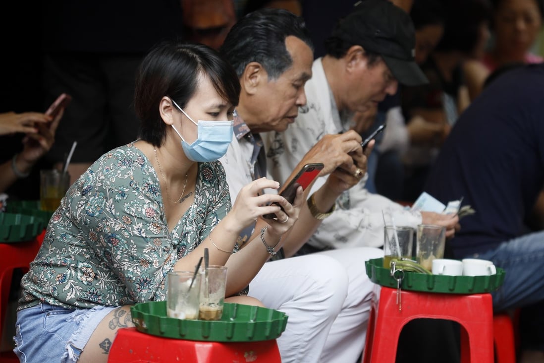 A woman wearing a mask checks her mobile phone at a street cafe in Hanoi. Vietnam has contained the coronavirus faster than much of Asia. Photo: EPA-EFE