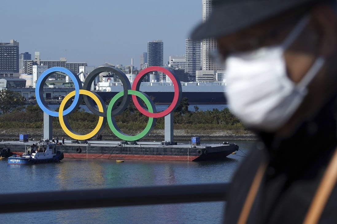 A man wearing a protective face mask to help curb the spread of the coronavirus walks past the Olympic rings in Tokyo. Photo: AP