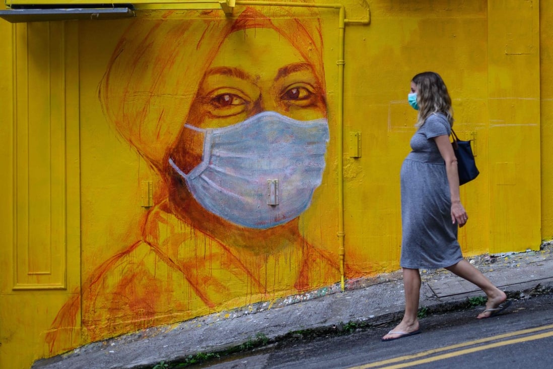 A pregnant woman wearing a face mask walks past a street mural in Hong Kong in March 2020. Photo: AFP