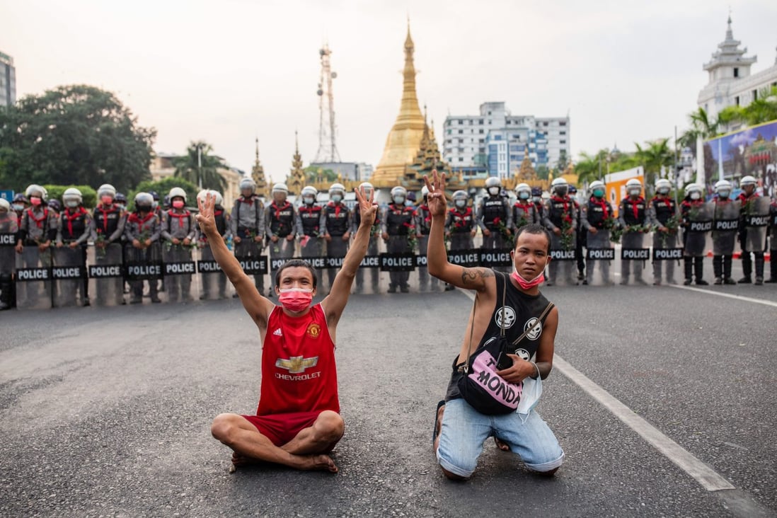 Protesters display the three-fingered salute in front of police officers at the Sule Pagoda. Photo: dpa