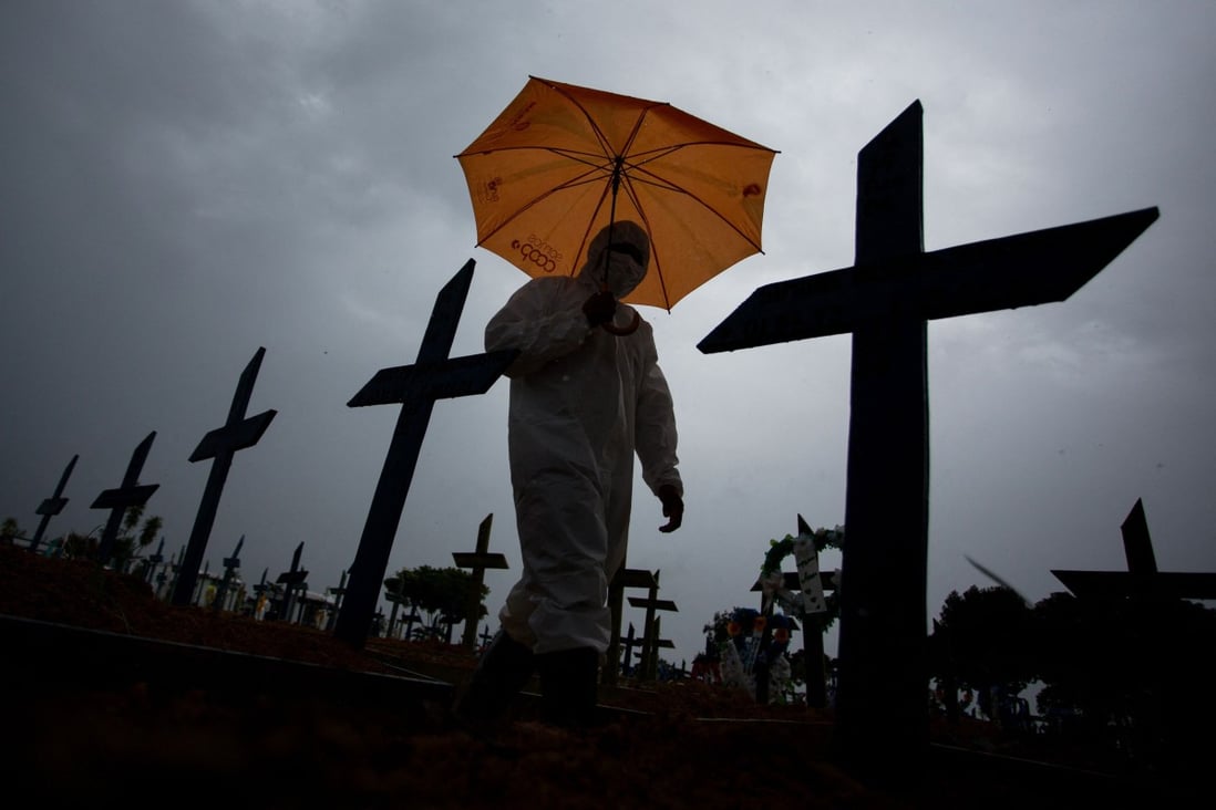 A worker wearing a protective suit and carrying an umbrella walks past the graves of Covid-19 victims at the Nossa Senhora Aparecida cemetery in Manaus, Brazil on Thursday. Photo: AFP