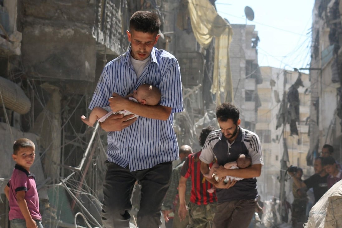 Syrian men carrying babies make their way through rubble after an air strike in the city of Aleppo in 2016. File photo: AFP