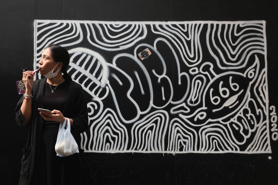 A woman on a vaping break in front of a graffiti art piece in Causeway Bay on September 17, 2020. Photo: Xiaomei Chen