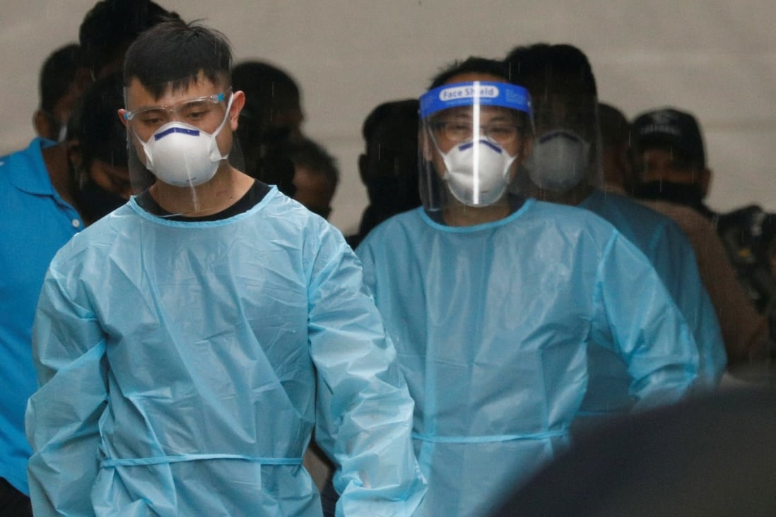 Personnel in protective gear usher a group of migrant workers to take a bus to a quarantine facility in Singapore. Photo: Reuters