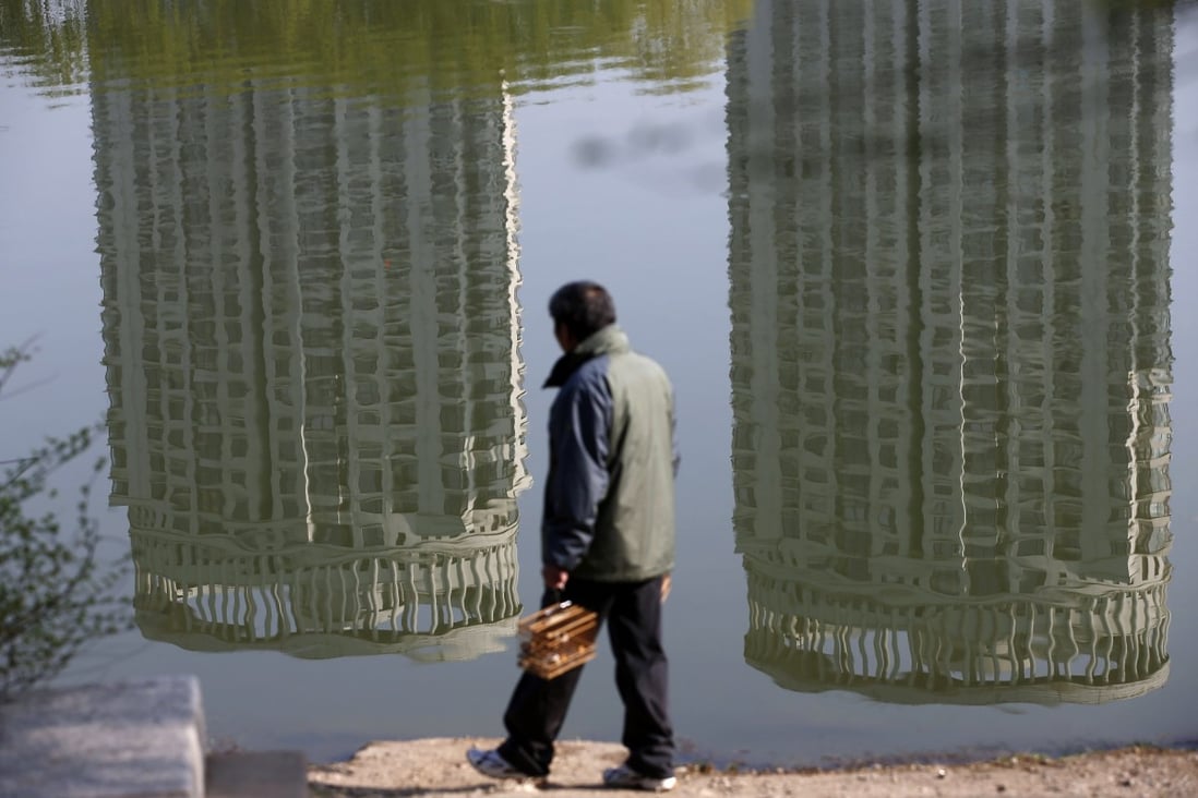 A man walks past the reflection of residential buildings in a park in Shenyang, Liaoning province. The housing market is seeing rising vacancy rates in cities including Dalian, Harbin and Shenyang. Photo: Reuters