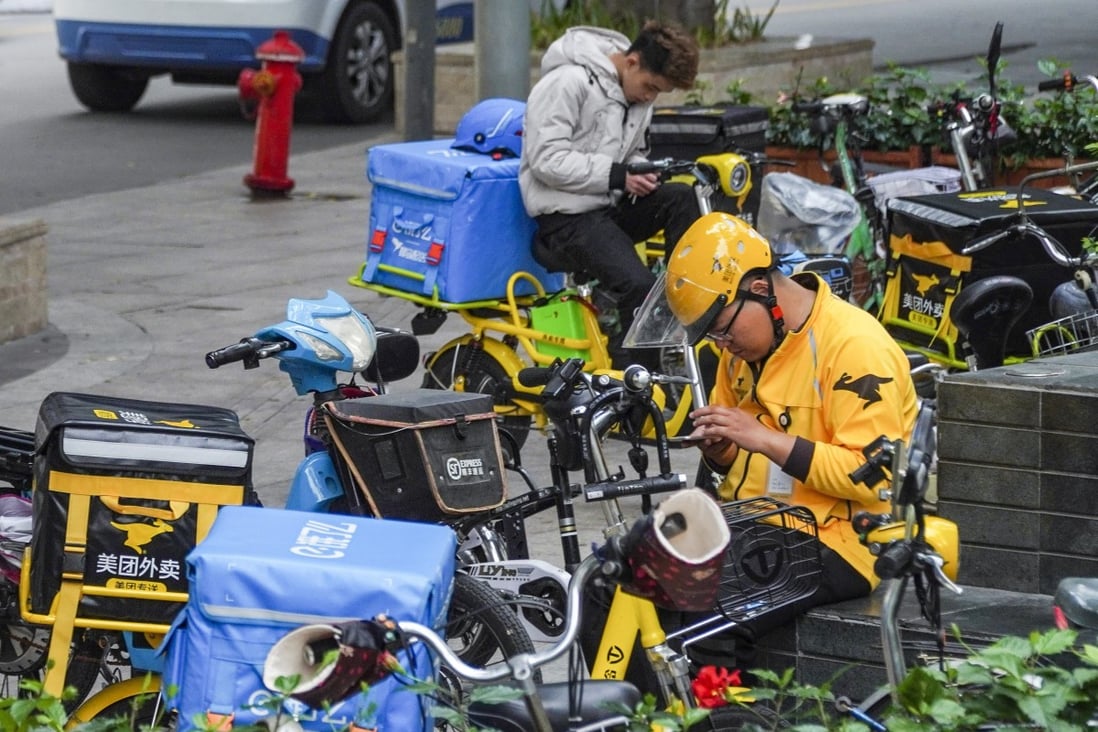 A delivery driver for Meituan, wearing a yellow helmet, and another driver from rival on-demand service provider Ele.me, at the back, are seen checking their smartphones, while on standby in the Futian district of Shenzhen. Photo: SCMP