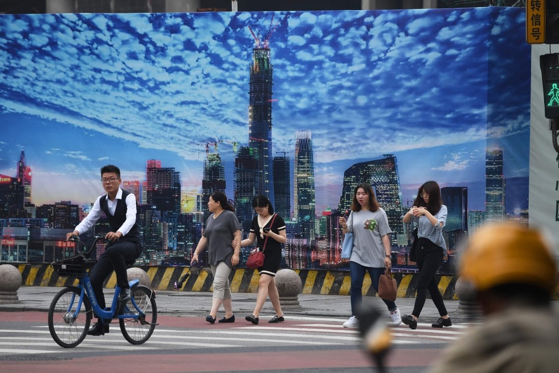 People crossing a road in front of a billboard on the wall of a construction site in Beijing's central business district in July 2018. Slower growth in China is fanning bets on policy easing. Photo: AFP