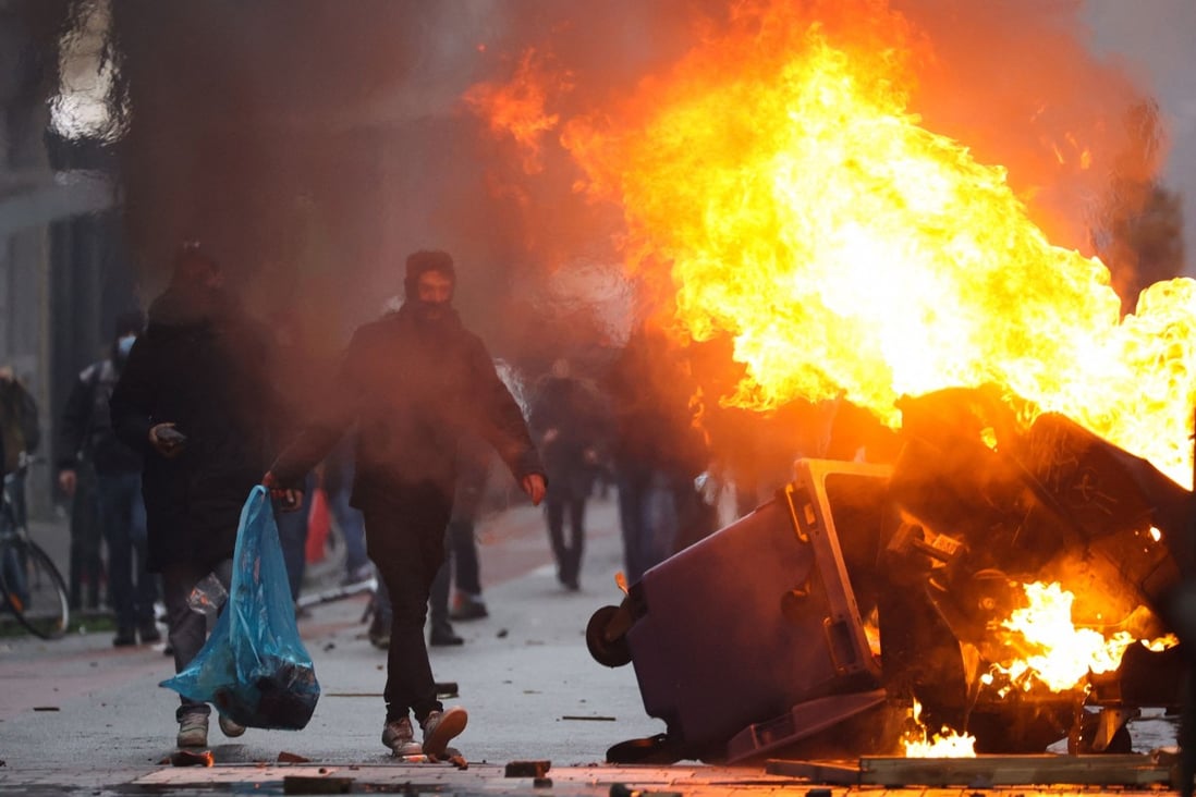 A protester walks past burning rubbish as clashes erupt during a demonstration against Covid-19 measures in Brussels, Belgium on Sunday. Photo: AFP