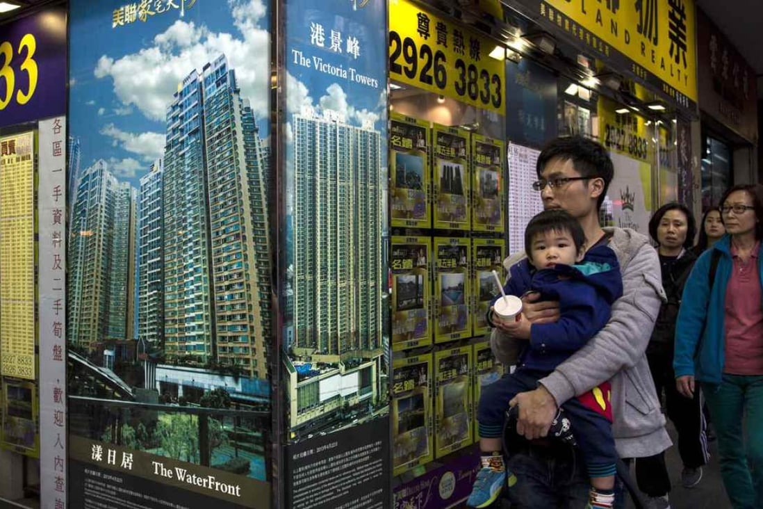 A man carrying a boy walk outside a property agency featuring posters of the latest high-rise apartment buildings in Hong Kong . Photo: Reuters