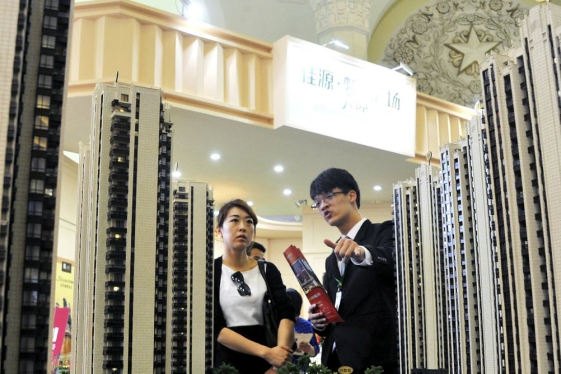 A sales assistant (R) speaks to a customer in front of a model of a residential complex, at a real estate exhibition in Shanghai, China. Photo: Reuters