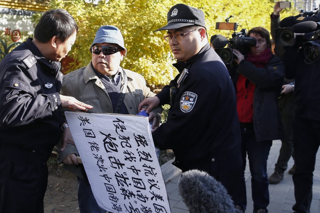 A protester with a sign that reads 'Strongly protest against US encroachment on South China Sea is held by two police outside the US Embassy in Beijing on October 28. Photo: EPA