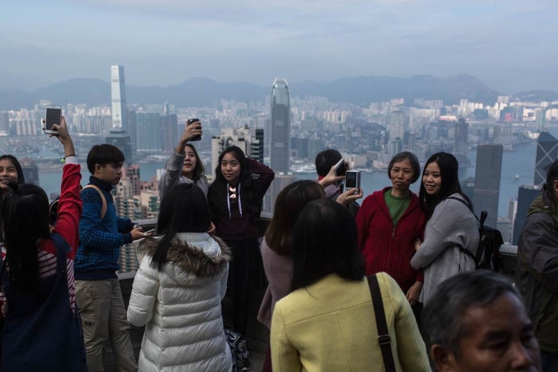 Tourists take pictures at the Peak in front of the city skyline and Victoria harbour in Hong Kong on December 26. Photo:
