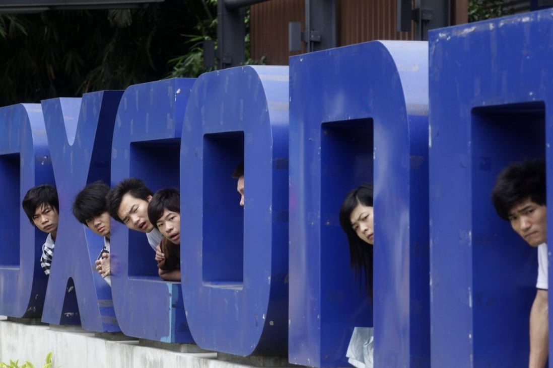 Workers look on from a Foxconn logo near the gate of a Foxconn factory in the township of Longhua, Guangdong province. The once controversial firm is back in favour with job seekers who are faced with a toughening market. Photo: Reuters