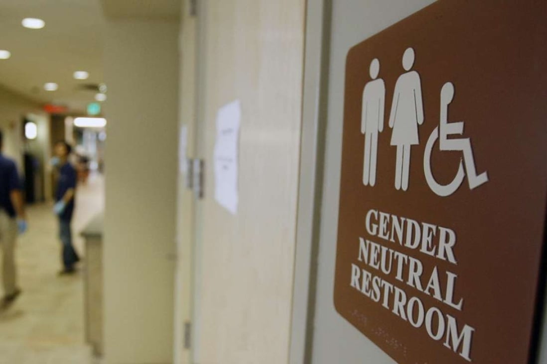 A gender-neutral restroom sign on a door indicates inclusive facilities, with the background showing a hallway in what appears to be a public building or transportation hub.