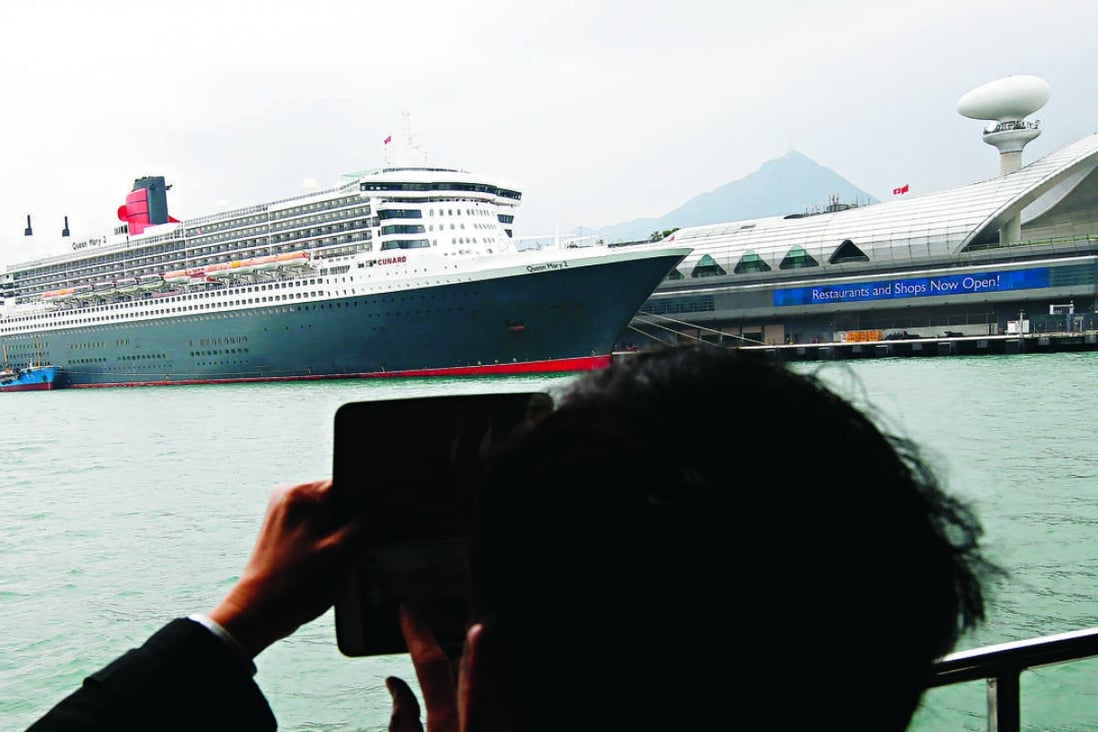 A man takes a picture of Queen Mary 2 while it is docked at the cruise terminal at Kai Tak. Photo: David Wong