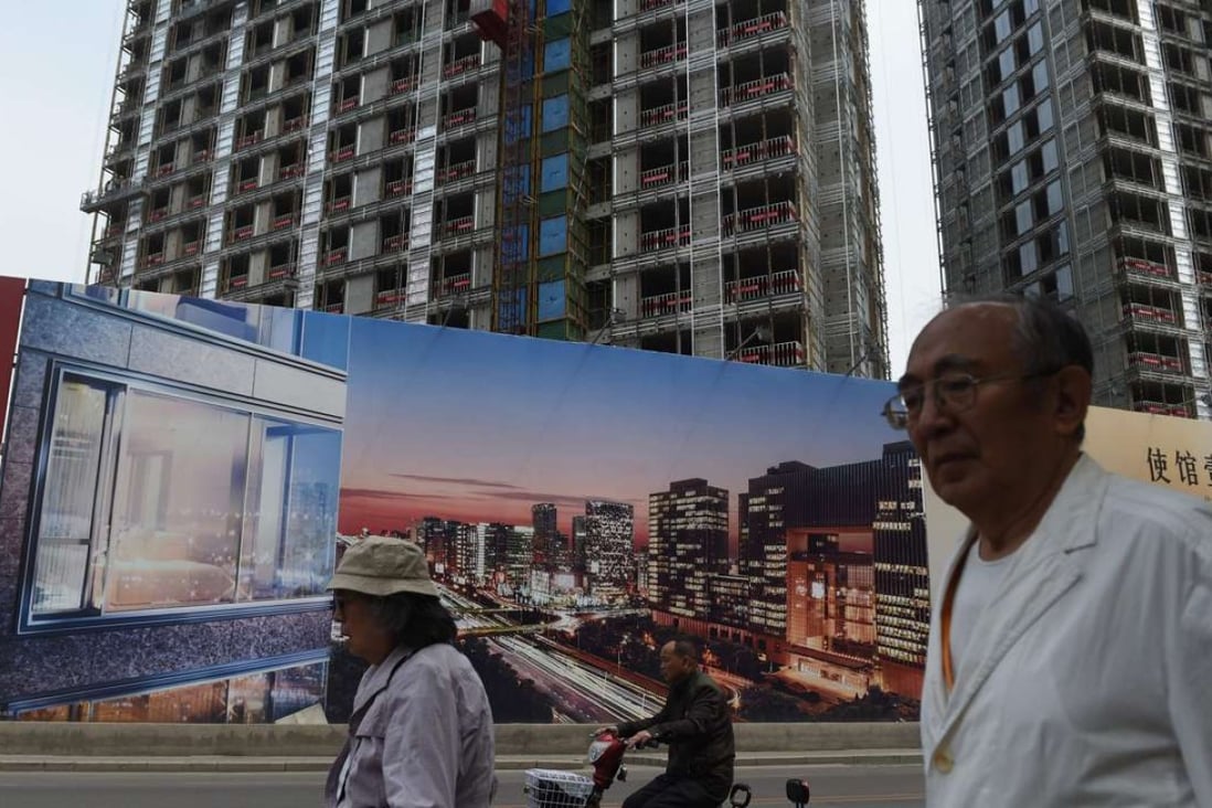 People walk past a billboard advertising a new housing complex outside a construction site in Beijing. Photo: AFP