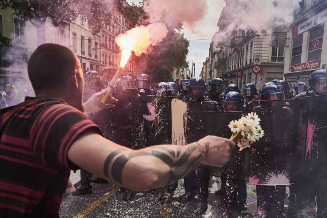 A man holds a bouquet of flowers and a torch as he faces riot police during a demonstration against the government's planned labour reform, on May 26, 2016 in Lyon, central eastern France. Photo: AFP