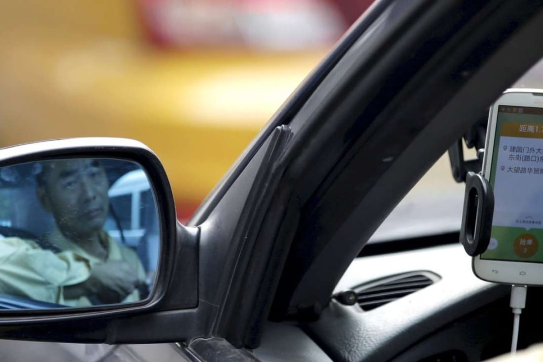 A driver is reflected in a side mirror as he uses the Didi Chuxing car-hailing application. Photo: Reuters
