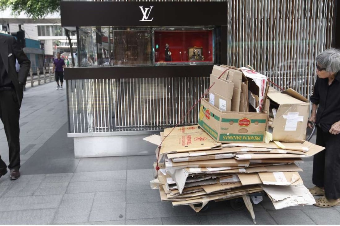 An elderly low-income earner pushes a trolley with cardboard bundles for recycling past a luxury designer boutique in Hong Kong's Central district. Photo: EPA