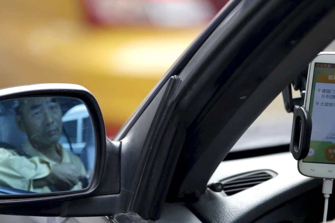 A taxi driver is reflected in a side mirror as he uses the Didi Chuxing car-hailing application in Beijing. Photo: Reuters