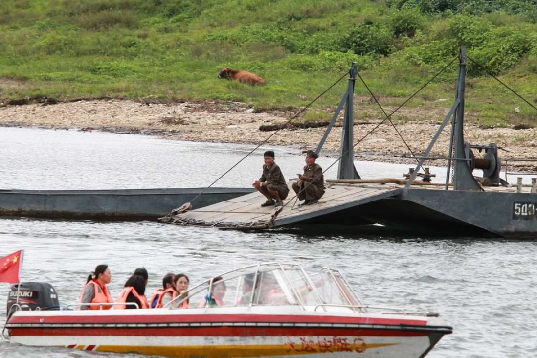 Two North Korean soldiers look at Chinese tourists taking a boat ride along an inner river in North Korea. Photo: Simon Song
