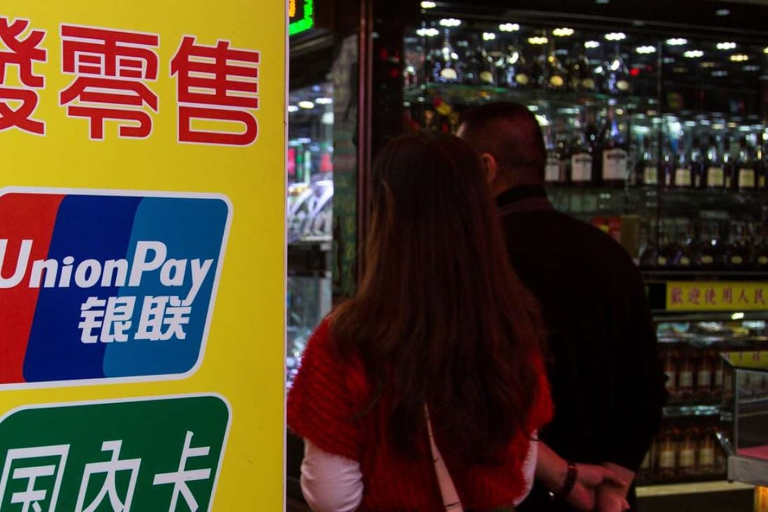 Chinese visitors walk past a sign for China UnionPay outside a pawnshop in Macau. Curbs on taking out cash in the former Portuguese enclave mark the latest move to curb the flow of money out of the mainland. Photo: Reuters