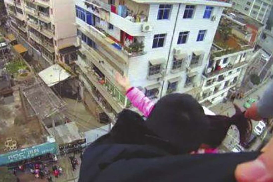 The husband holds on to his wife’s hair as a police officer tries to grab her. Part of her body weight was also supported by a pipe at the edge of the building. Photo: Sohu.com