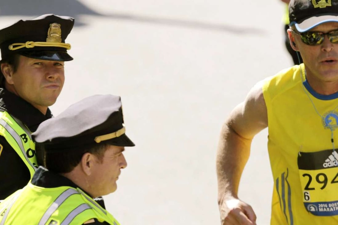 Actor Mark Wahlberg, left, dressed as a Boston Police officer, watches runners cross the finish line as he films a scene for his "Patriot's Day" movie about the 2013 Boston Marathon bombing. Photo: AP